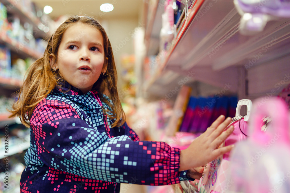 Small girl child looking at the toy picking present at the shelve of the shop ardor face