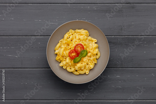 A bowl of delicious Macaroni and cheese, topped with cherry tomatoes and basil, on a distressed wooden background.