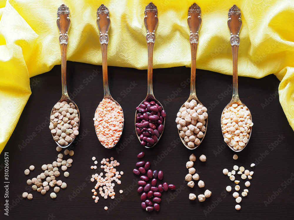 Beans, lentils, yellow peas, chickpeas in gold tablespoons with a yellow  napkin on a black background closeup. Colorful picture with vegetarian  legumes for decoration and design, top view. Stock Photo | Adobe