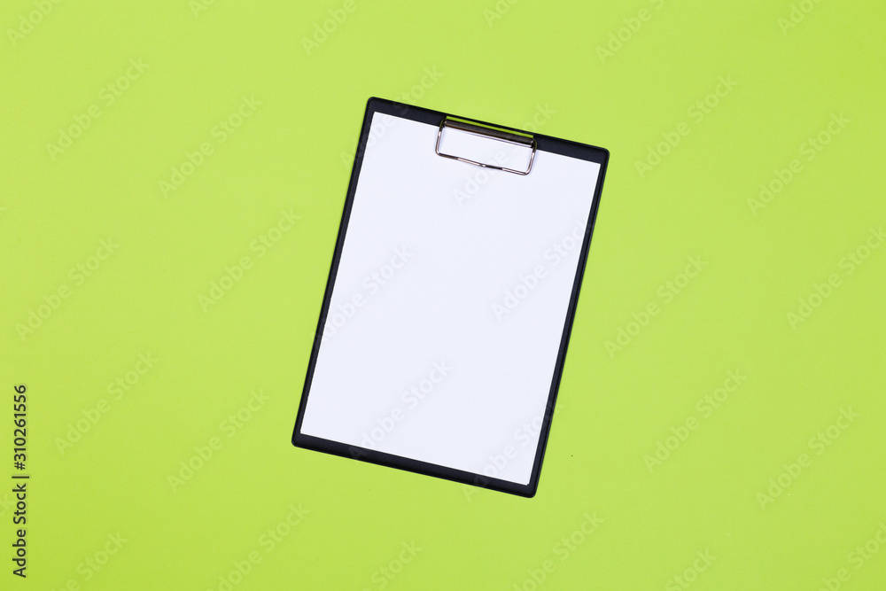 Clipboard with white sheet and pen on a green background. View from above. space for text Clipboard with white sheet and pen on a green background. View from above. space for text