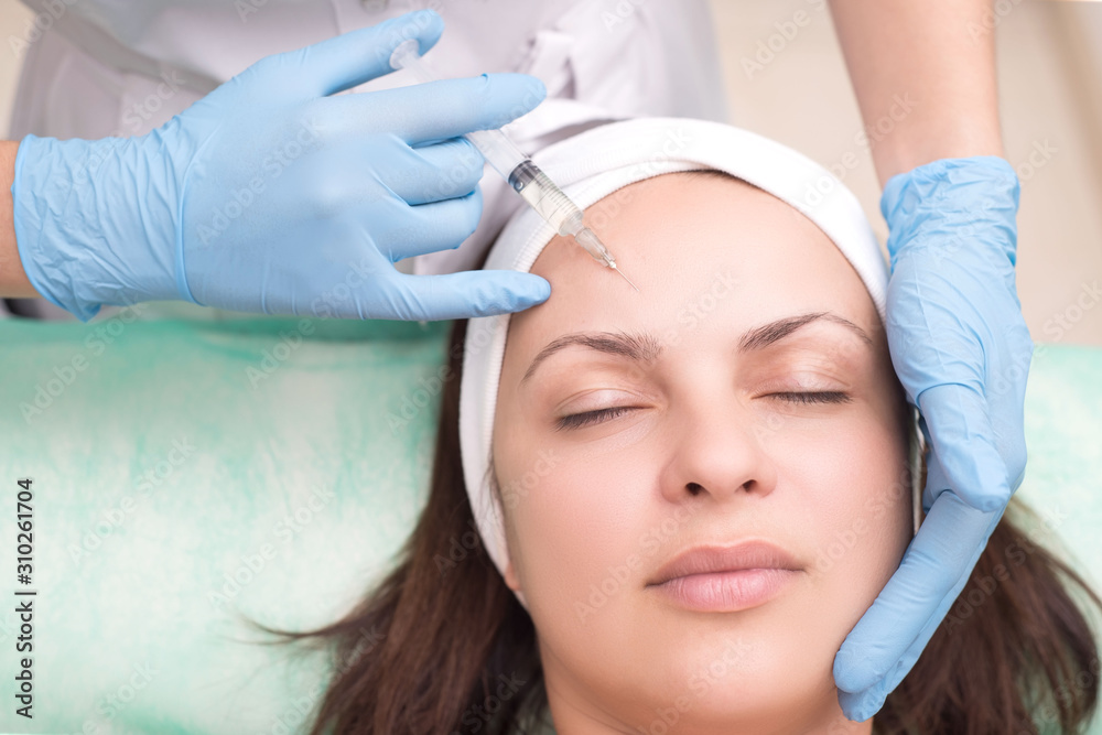 injection into the skin of the face of a young woman, close-up. Beautician with a syringe with a needle introduces a tool to remove wrinkles on the face in the eyebrow area. injection into the skin of the face of a young woman, close-up. Beautician with a syringe with a needle introduces a tool to remove wrinkles on the face in the eyebrow area.