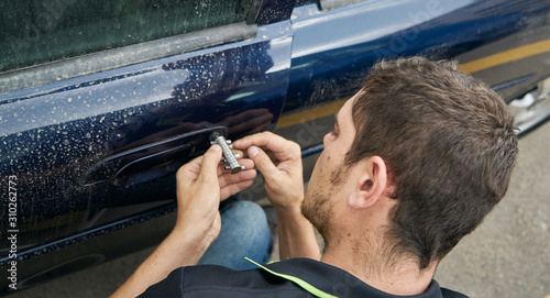 Locksmith opening with the lockpicker a blue car that its owner has lost the keys
