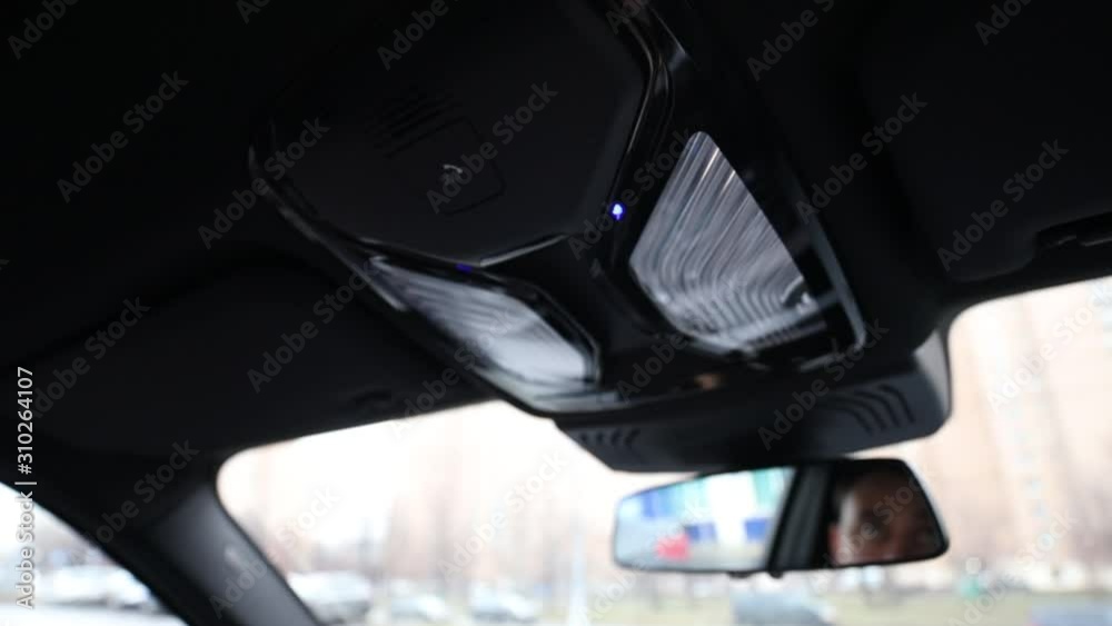 A man, a car driver clicks on the SOS button which is on the ceiling