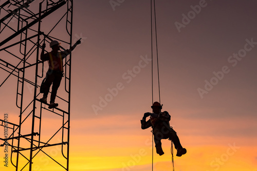 silhouette construction team working on high ground over blurred background sunset sky.