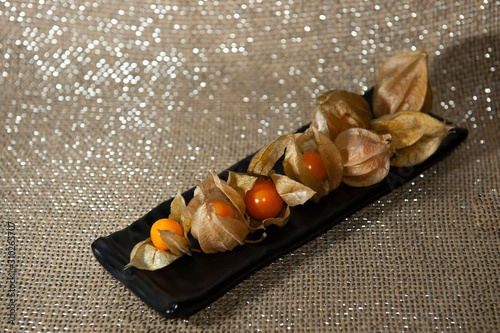 Fruits physalis, in rectangular plate, black, diagonally. Selective focus. Brazilian natal table. Jute background with white lights. Seen from above. Horizontal. photo