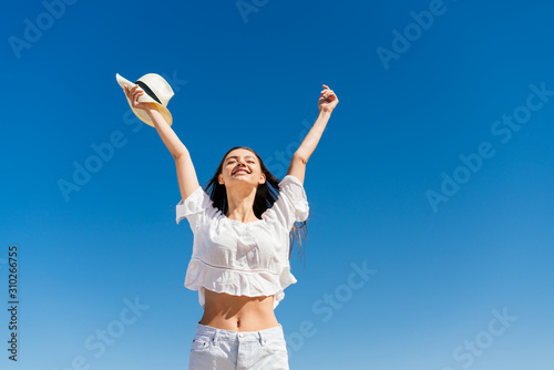 girl with a hat in her hand joyfully triumphantly threw up her hands against a blue sky