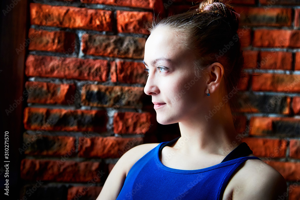 Flexible beautiful gymnast girl standing near wall with red brick and waiting performance. Portrait of young woman in sport dress. Posing of model