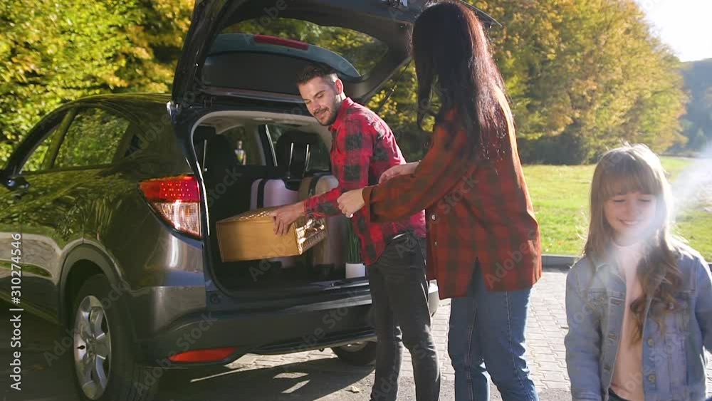 Happy cheerful family unloading the car's trunk during their relocation to the new apartment