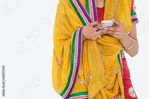Midsection of woman in Indian clothing using cell phone over gray background