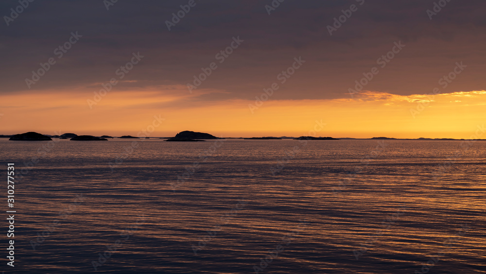 colorful orange sunset under dark sky over the sea above the arctic circle in norway shot from a boat with a view oves of Norway on a sunny day in spring within a beautiful landscape shot from a boat 