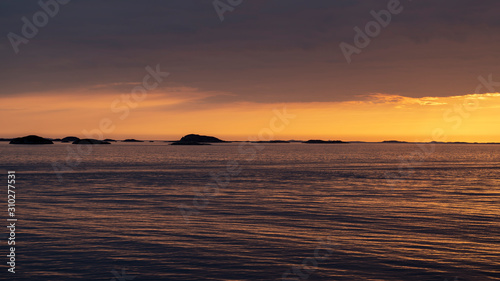 colorful orange sunset under dark sky over the sea above the arctic circle in norway shot from a boat with a view oves of Norway on a sunny day in spring within a beautiful landscape shot from a boat 