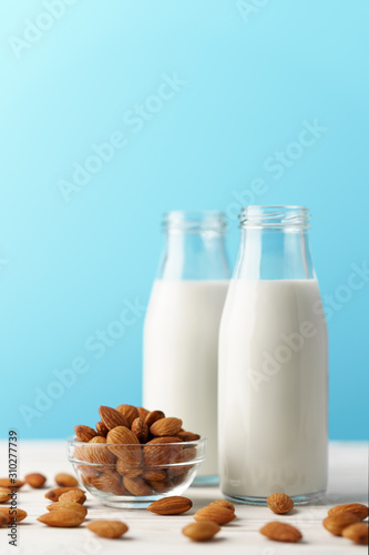 Two glass reusable bottles with almond milk. Almond nuts lie on a white wooden table and a blue background.