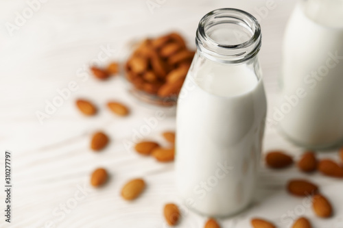 Close-up of almond milk in reusable glass bottles  almond nuts on a white wooden table lie nearby.