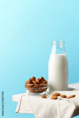 Glass reusable bottle with almond milk  almond nuts lie nearby  textile napkin on a white wooden table and a blue background.