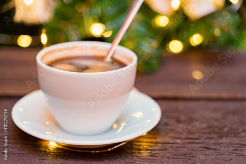 Cup of coffee with spoon with Christmas lights blur in background