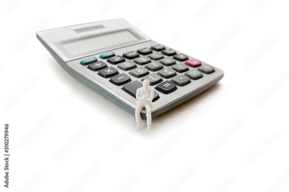 A small dummy figure sitting on a calculator over white background A small dummy figure sitting on a calculator over white background