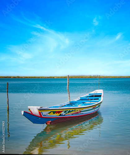 Traditional colorful wooden boat on the river in sea lagoon and a beautiful sky in the background, Africa, Senegal.