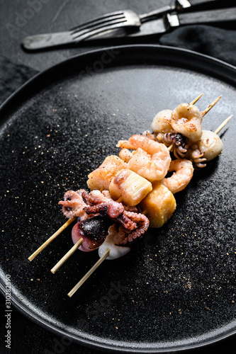 Wooden skewers with shrimp, octopus, squid and mussels. Kebab with seafood. Black background. Top view
