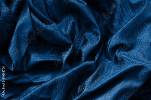 Closeup classic blue macro texture of shiny smooth material fabric or clothing. Toned trendy 2020 year color background with wrinkles, folds. Dark blue monochrome backdrop wallpaper.