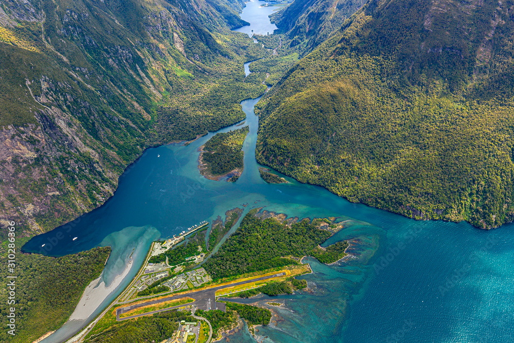 New Zealand. Milford Sound (Piopiotahi) from above - the head of the fiord with wharf and Milford Sound Airport. There is Arthur River and Lake Ada in the background