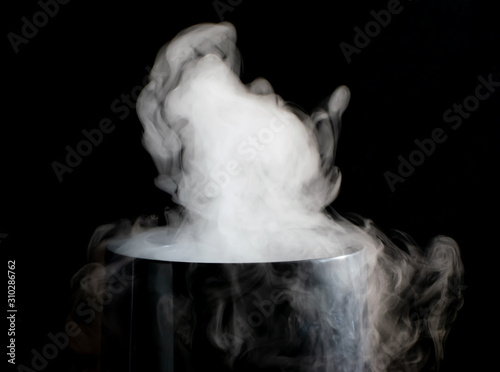 Puffs of white smoke randomly rising rise from the chimney partially flowing down its edges on a black background