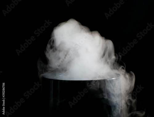 Puffs of white smoke randomly rising rise from the chimney partially flowing down its edges on a black background