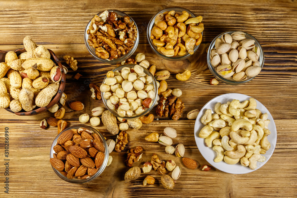 Assortment of nuts on wooden table. Almond, hazelnut, pistachio, peanut, walnut and cashew in small bowls. Top view. Healthy eating concept Assortment of nuts on wooden table. Almond, hazelnut, pistachio, peanut, walnut and cashew in small bowls. Top view. Healthy eating concept