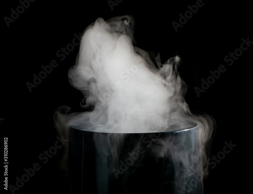 Puffs of white smoke randomly rising rise from the chimney partially flowing down its edges on a black background