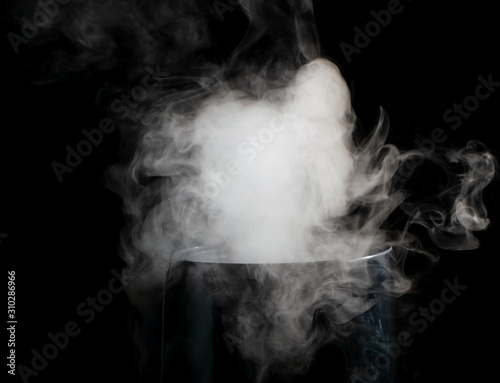 Puffs of white smoke randomly rising rise from the chimney partially flowing down its edges on a black background