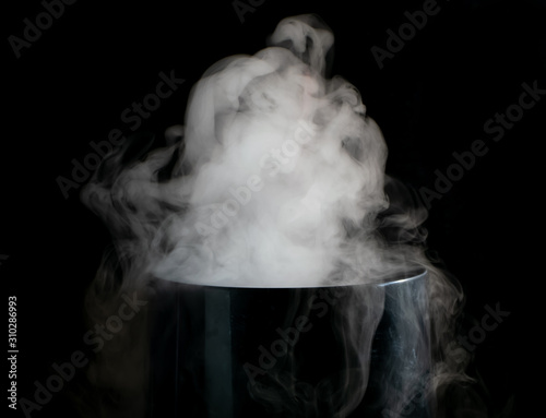 Puffs of white smoke randomly rising rise from the chimney partially flowing down its edges on a black background