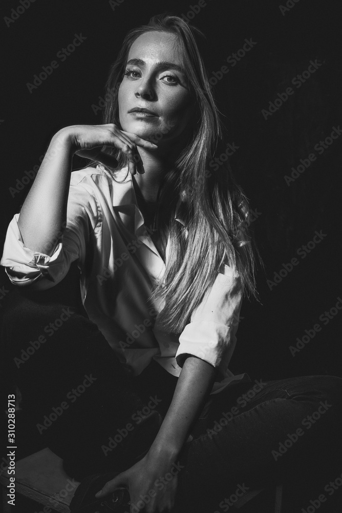 Art black and white portrait of a beautiful girl in a white shirt. Fashionable advertising photo of a young woman on a dark background