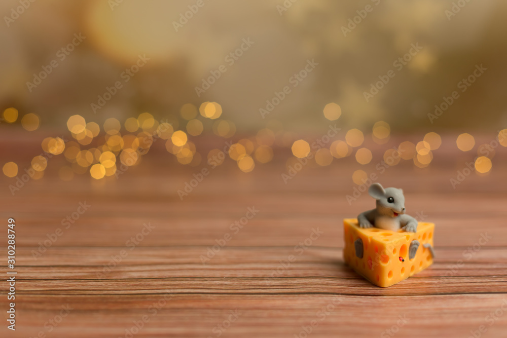 A toy mouse sits in cheese on a wooden starry background, a symbol of 2020. A toy mouse sits in cheese on a wooden starry background, a symbol of 2020.