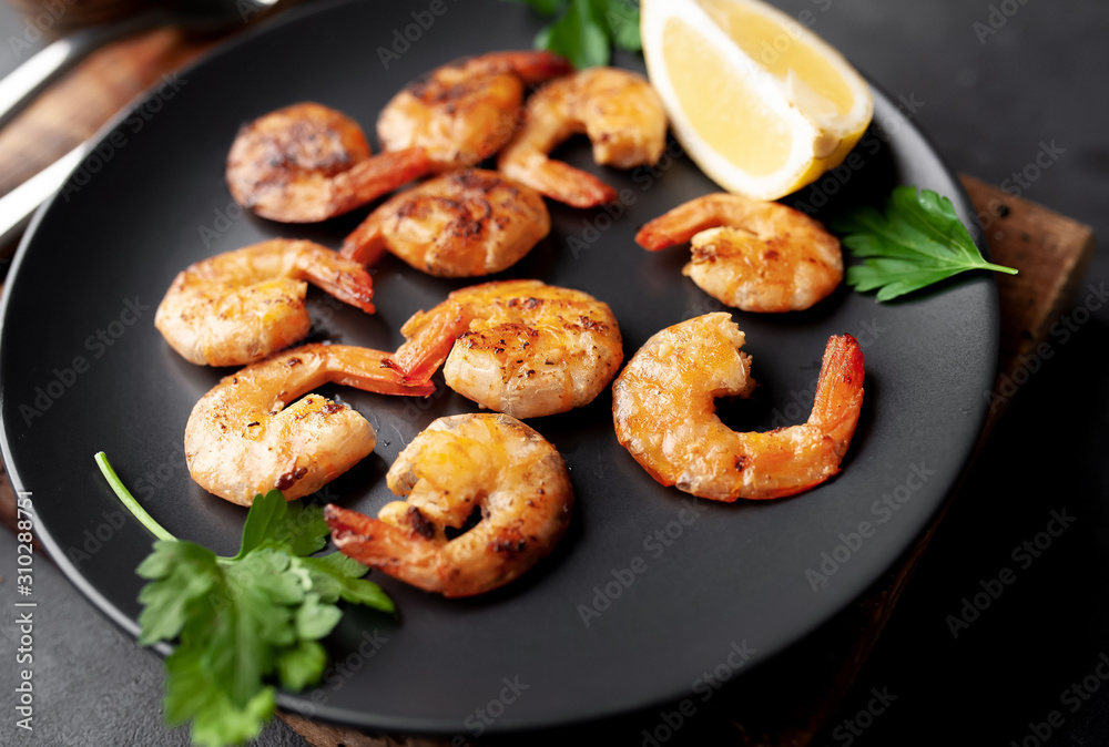 grilled shrimps, with lemons, herbs and spices, served on a black plate on a stone background grilled shrimps, with lemons, herbs and spices, served on a black plate on a stone background