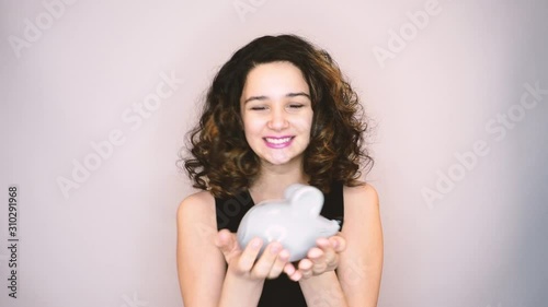 Smiling girl brunette shaking piggy-bank, listening to ringing of coins, deposits. 4k