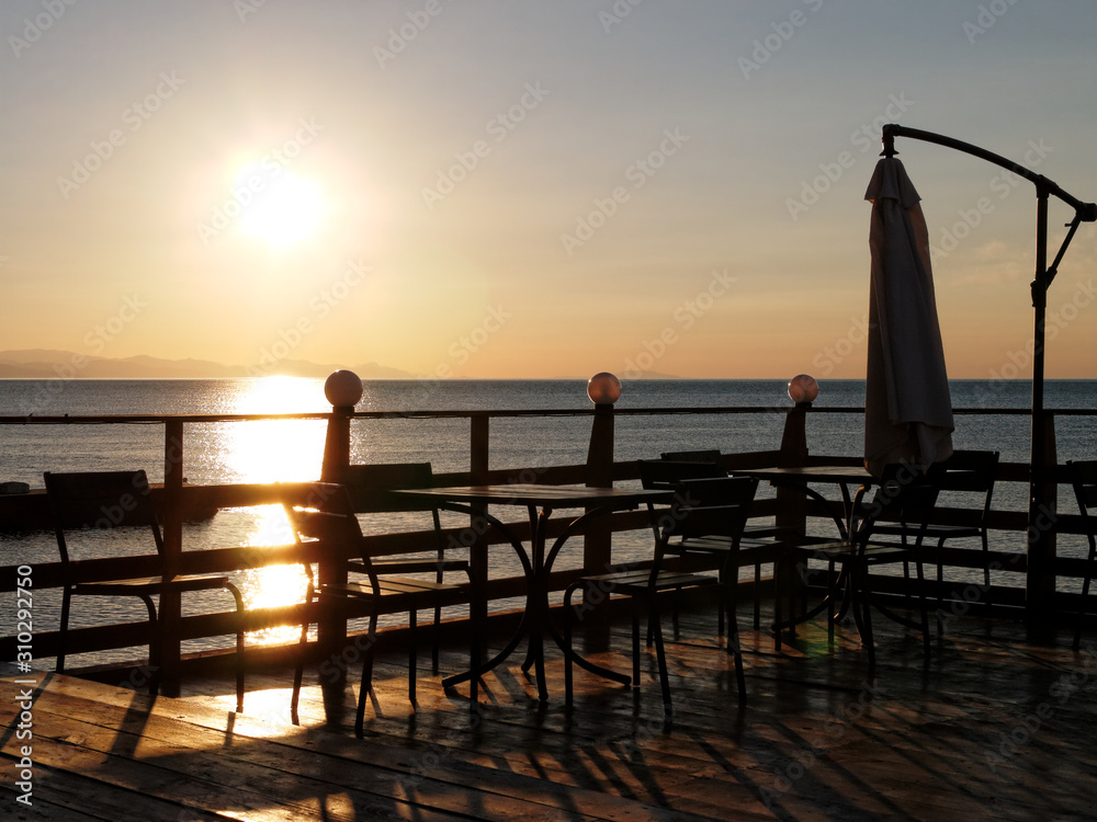 summer cafe with tables and chairs at sunrise opposite sunny path to the sea and the mountains in the background      