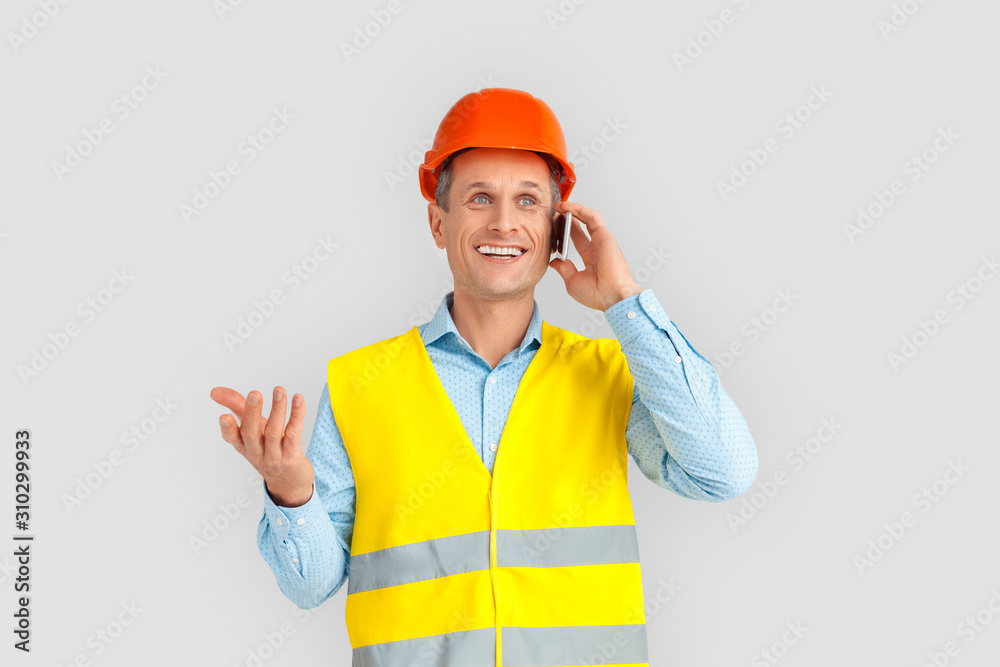 Construction. Mature man in hardhat and uniform standing isolated on white talking with friend on smartphone joyful