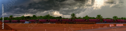Tropical rainstorm over railway carriages for bauxite ore transportation on train tracks at the end of the railway line from bauxite mining. Guinea, Africa. photo