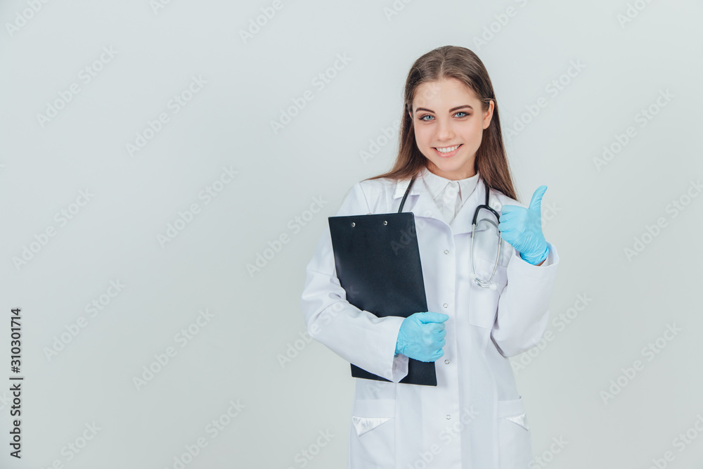 Inspired young female intern standing in medical uniform, holding clipboard, giving thumb up, showing her approval. Inspired young female intern standing in medical uniform, holding clipboard, giving thumb up, showing her approval.