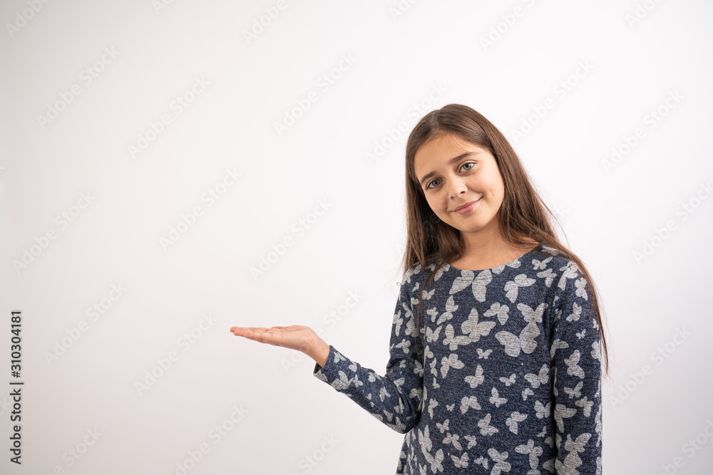 Waist up portrait of the attractive young brunette girl in blue dress that stands with raised opened palm, holds your product and looking at the camera, isolated over white background Waist up portrait of the attractive young brunette girl in blue dress that stands with raised opened palm, holds your product and looking at the camera, isolated over white background