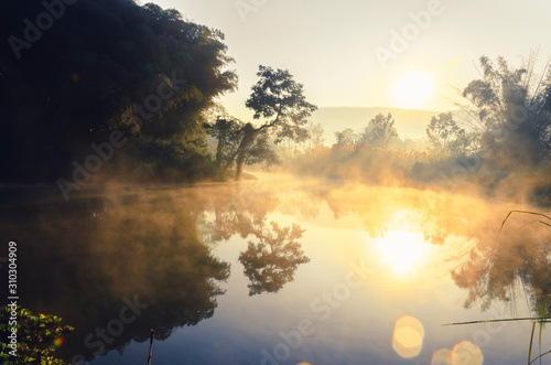 The beautiful landscape of the sunrise, The sun's rays through at the top of the hill and There is steam above the river, with beautiful Water reflection trees, Chiang Rai Thailand