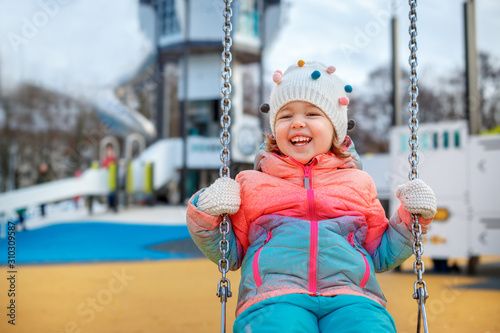 Adorable little girl on the playground. Toddler having fun on a swing on beautiful winter day