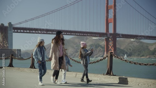 Girl walking near Golden Gate Bridge with family and photographing scenic view / San Francisco, California, United States