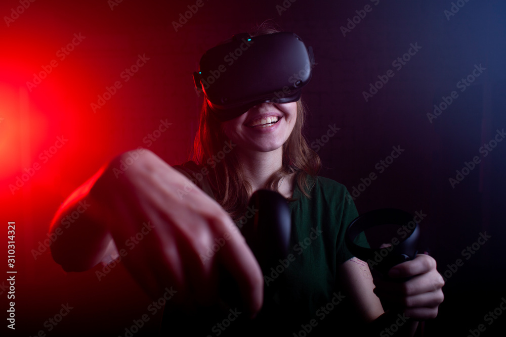 girl gamer in modern wireless virtual reality glasses plays a shooter on a dark red-blue background, a woman shoots with game joysticks girl gamer in modern wireless virtual reality glasses plays a shooter on a dark red-blue background, a woman shoots with game joysticks