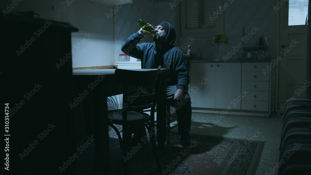 Alcoholic man drinks alone at his old dirty derelect house.A depressed secluded and addicted caucasian adult male is drinking heavily sitting down at his kitchen table. Alcoholic man drinks alone at his old dirty derelect house.A depressed secluded and addicted caucasian adult male is drinking heavily sitting down at his kitchen table.