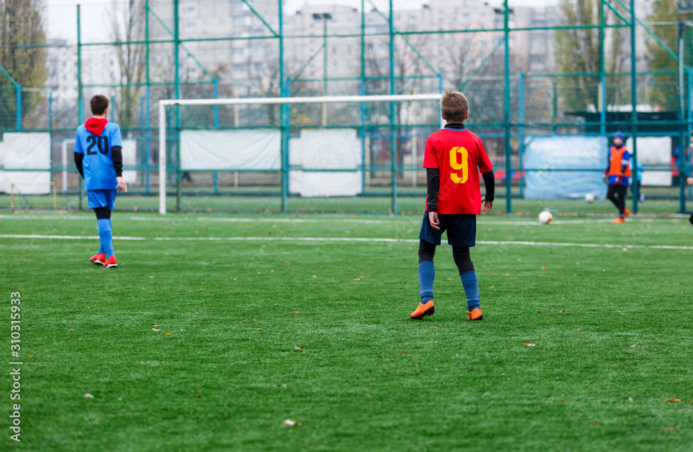 Obraz premium Boys in red and blue sportswear plays football on field, dribbles ball. Young soccer players with ball on green grass. Training, football, active lifestyle for kids concept