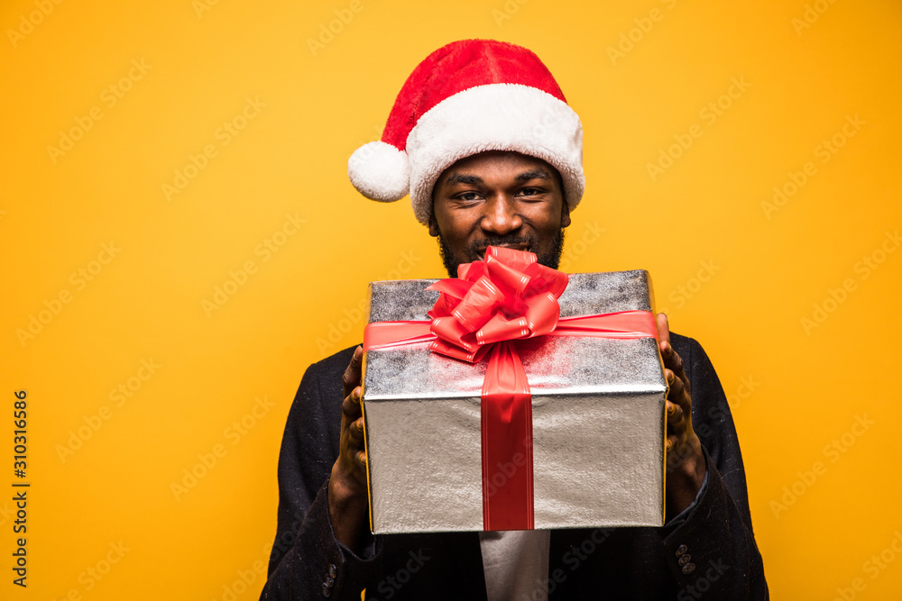 Portrait of handsome young man in santa hat with christmas presents isolated on yellow background Portrait of handsome young man in santa hat with christmas presents isolated on yellow background