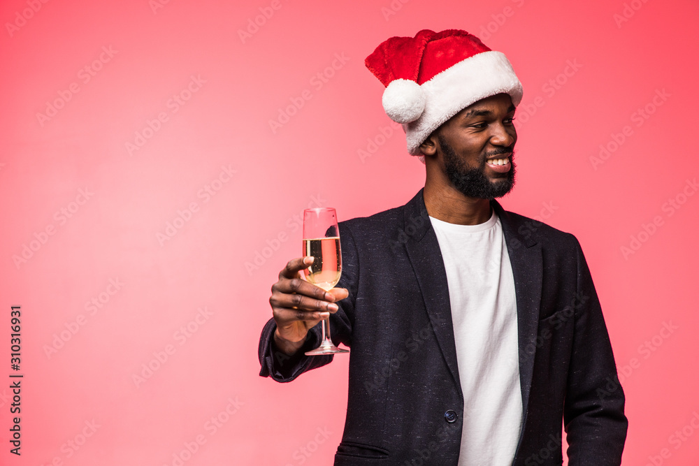 Young african man in santa hat drinking champagne isolated on red background Young african man in santa hat drinking champagne isolated on red background