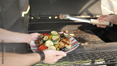 Grilled vegetables are removed from the grill and put on a plate. Vegetables and meat sausages grilled over charcoal photo