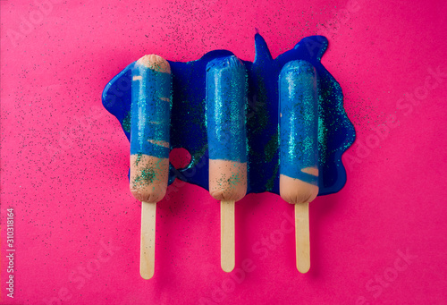 Sausages on sticks in blue sparkle paint. On a pink background, top view photo.