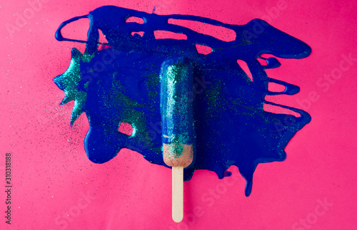 Sausage on sticks in blue sparkle paint. On a pink and orange textured background, top view photo.